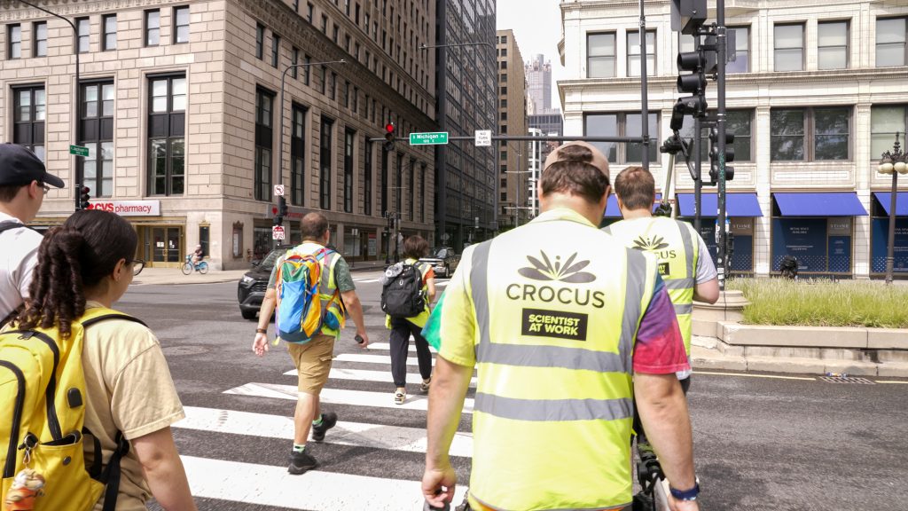 CROCUS researchers cross Chicago’s Michigan Avenue as they collect data on how buildings, streets and greenspaces impact temperature and air quality. They wear bright yellow safety vets with the CROCUS logo that reads 'Scientist at Work'